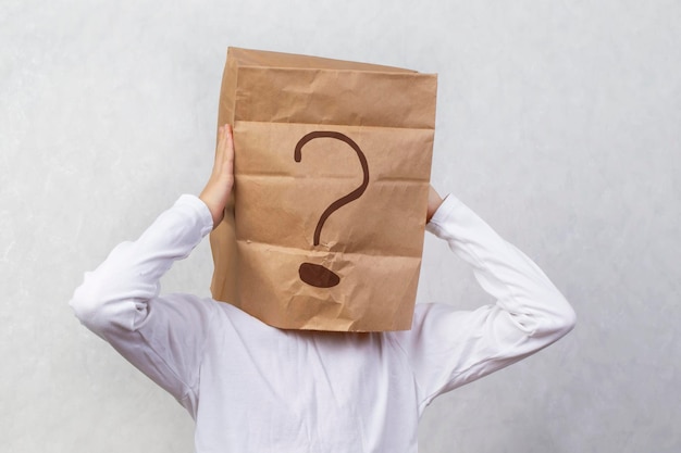 Anonymous man on a gray background with a cardboard box on his head with a drawn question mark