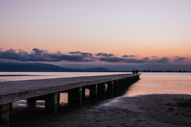 Anonymous persons sitting on pier near sea at sunset