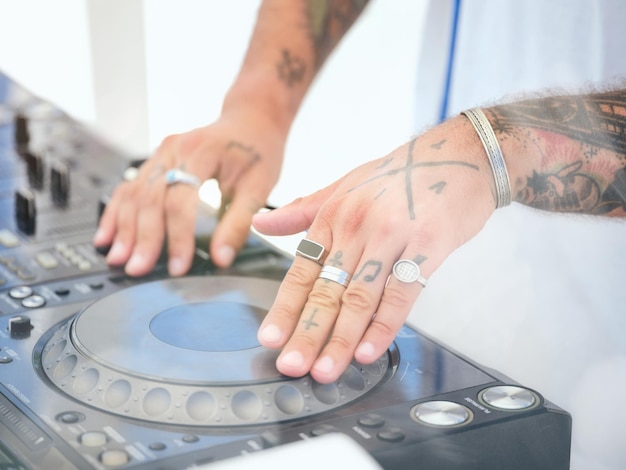 Anonymous tattooed disc jockey wearing craft silver accessories standing at DJ controller and mixing music