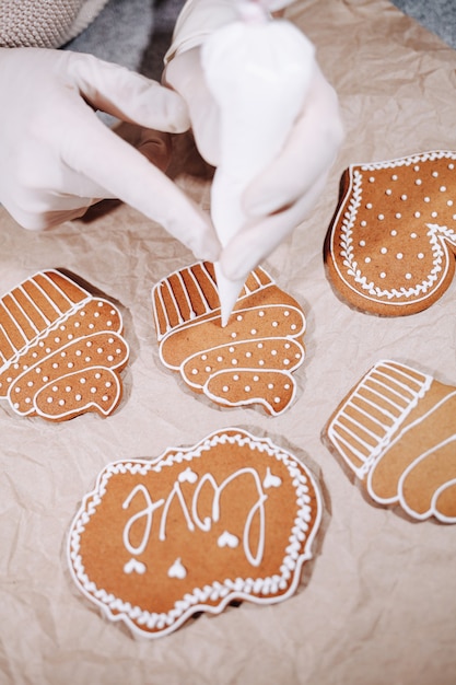 Photo anonymous woman decorating some homemade gingerbread cookies at kitchen