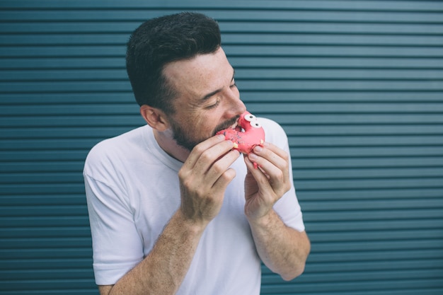 Another picture of man biting a piece of red donut. He likes sweets. Isolated on striped 