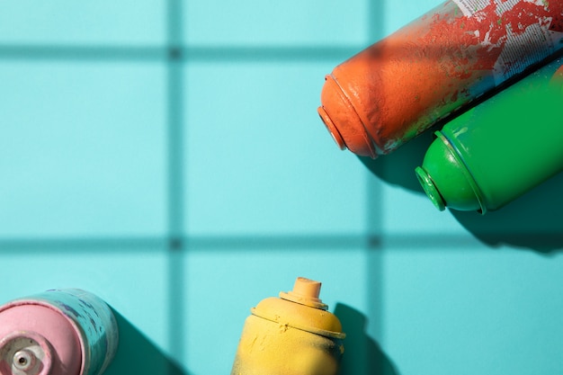 Another top view of used spray paint cans on cyan background with grid shadows and free space for text