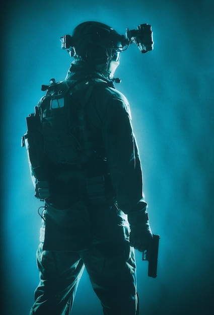 Anti terrorist squad fighter, army elite forces soldier in mask, with night vision device and tactical radio headset on helmet, armed service pistol standing ready for action, low key studio shoot