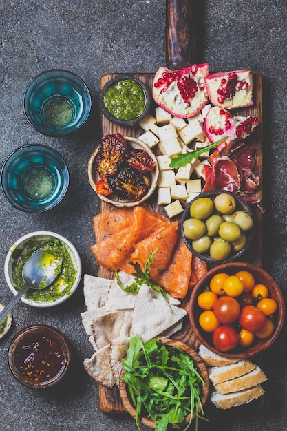 Photo antipasto wine set appetizer ham serrano smoked salmon dried and fresh tomatoes olive cheese wine on board top view gray cncrete background