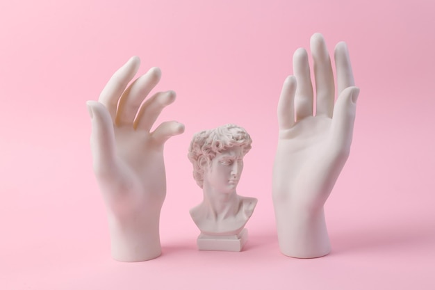 Antique bust of David with statues of hands on a pink background Minimal still life