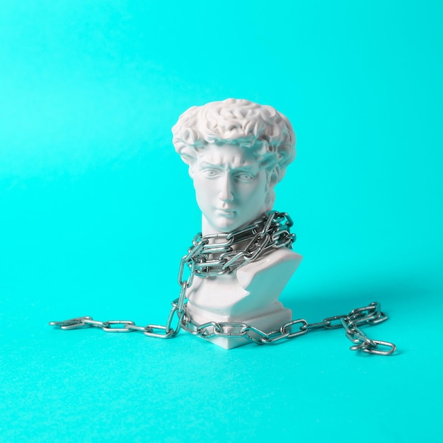 Antique bust of David wrapped steel chain on turquoise background Conceptual pop Minimal still life Creative idea