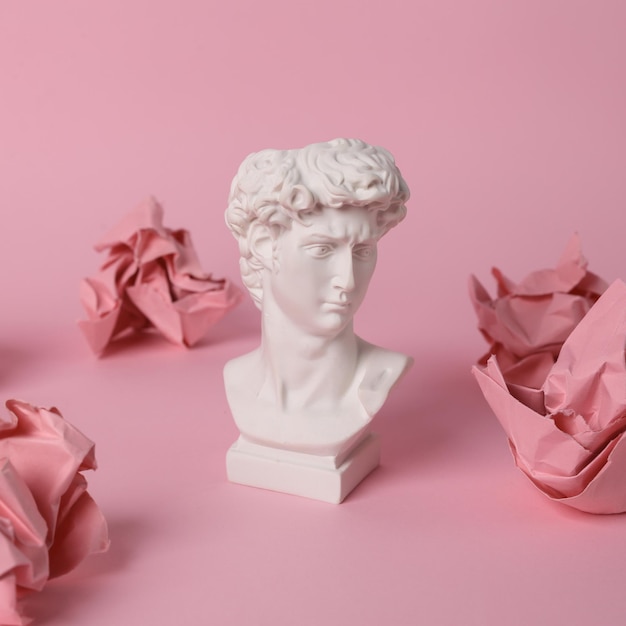 Antique David bust with crumpled paper balls on pink background Conceptual pop Minimal still life Creative idea