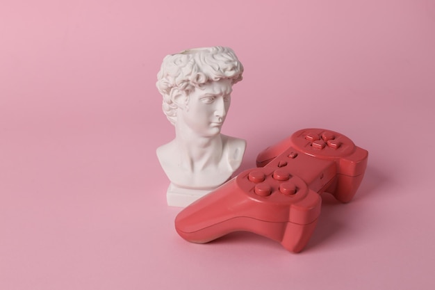 Antique David bust with gamepad on pink background Gaming Conceptual pop Minimal still life