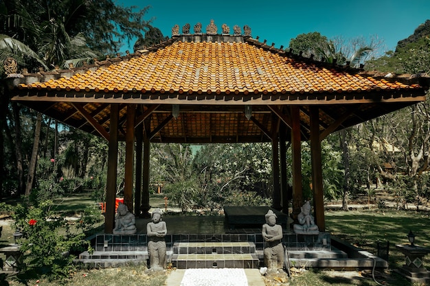 Antique gazebo pavilion with a roof asian style pagoda. In a summer tropical garden. A stone path along which the statues stand leads to the building. Inside the area of rest and meditation.