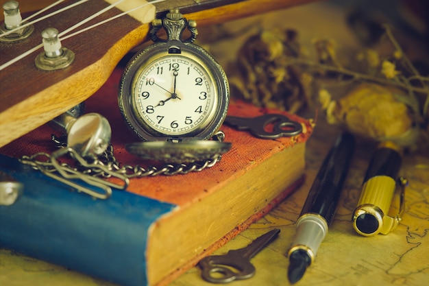 An antique pocket watch leaned against a ukulele and old book with vintage map