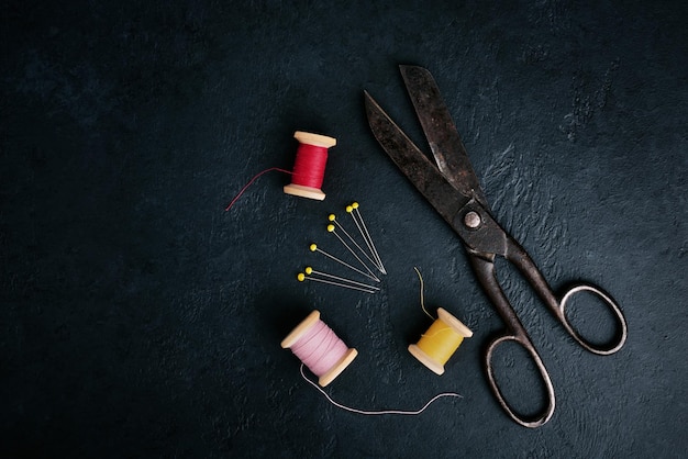 Antique rusty tailors scissors and thread on black background top view