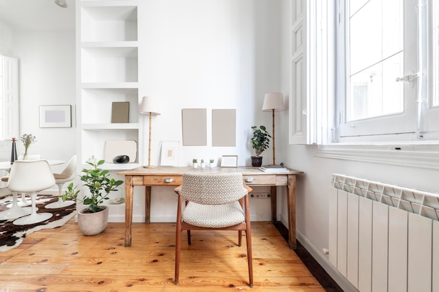 Antique wooden desk with upholstered chair and plaster bookcase next to a white wooden window