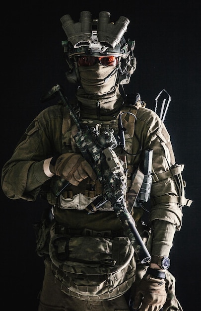 Antiterrorist squad fighter army elite forces soldier in combat uniform and tactical ammunition armed mini submachine gun wearing nightvision device low key studio portrait on black background