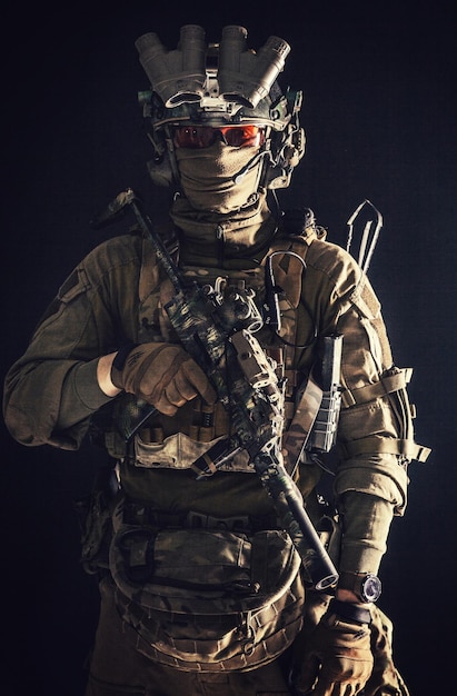 Antiterrorist squad fighter army elite forces soldier in combat uniform and tactical ammunition armed mini submachine gun wearing nightvision device low key studio portrait on black background