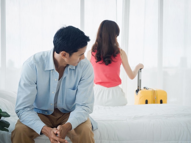 The anxiety of Asian couple lovers on the bed Stressed man and young woman sitting on the bed with baggage wants to go away with relationship difficulties and feeling sad in the bedroom at home