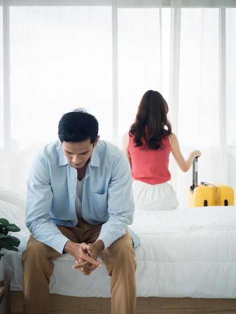 The anxiety of Asian couple lovers on the bed Stressed man and young woman sitting on the bed with baggage wants to go away with relationship difficulties and feeling sad in the bedroom at home