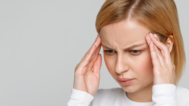 Anxiety attack, nervous tension. Close up portrait of woman with tense expression face touching her temples, tries to concentrate