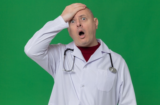 Anxious adult slavic man in doctor uniform with stethoscope putting hand on his forehead