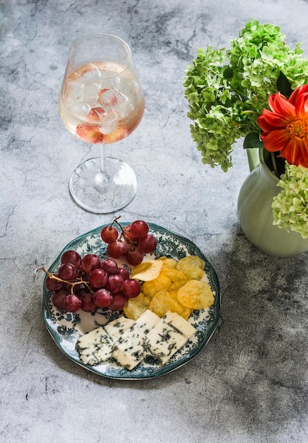 Aperitif cocktail and a plate with grapes cheese and chips on a gray background top view