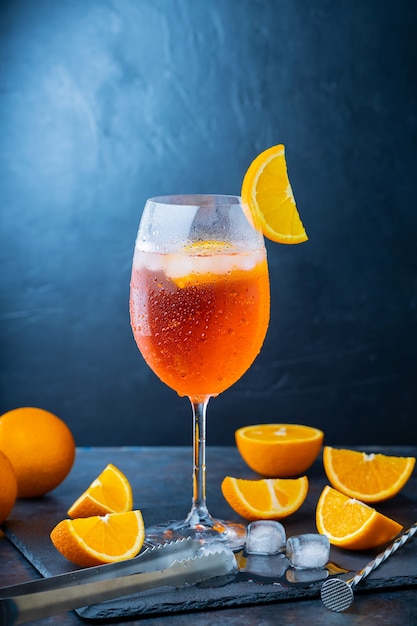 Aperol spritz cocktail and bar accessories. Italian aperol spritz cocktail and a sliced orange on a dark background. Summer cocktail aperol spritz on a slate board