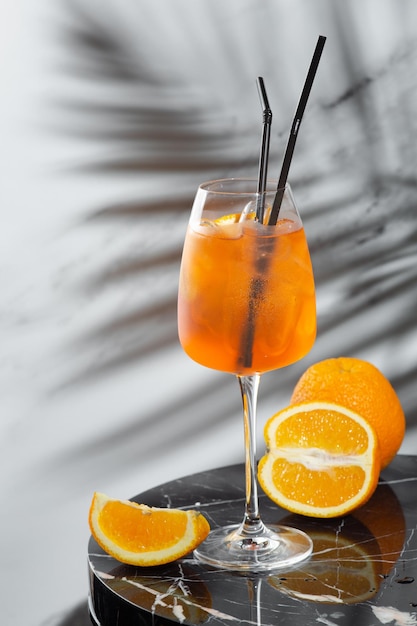 Aperol Spritz cocktail in glass and sliced orange on marble table. summer mood concept. cocktail with ingredients and shadow of branch on light background