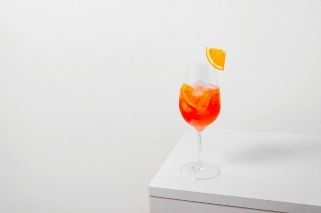 Aperol spritz cocktail in wine glass with ice and orange slice on white background