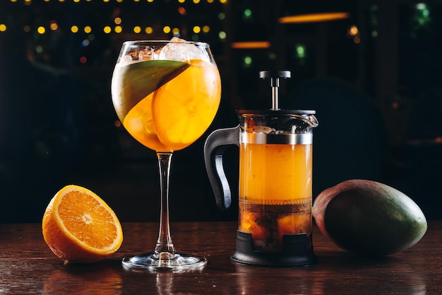 Aperol spritz and mango tea in french press on dark wooden background