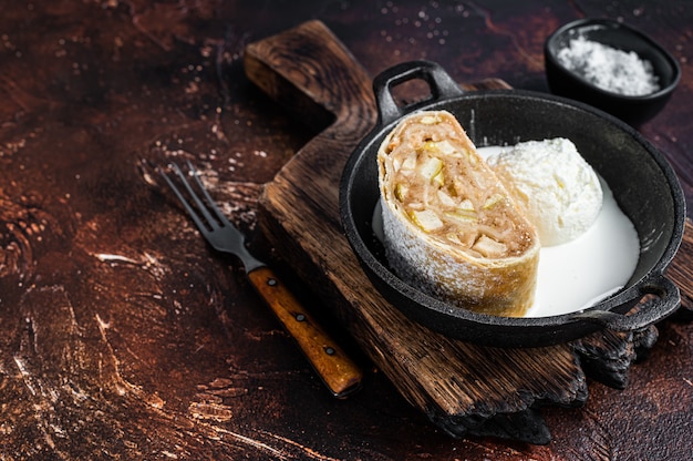 Apfelstrudel strudel with cinnamon, powdered sugar and vanilla ice cream in a pan. Dark background. Top view. Copy space.