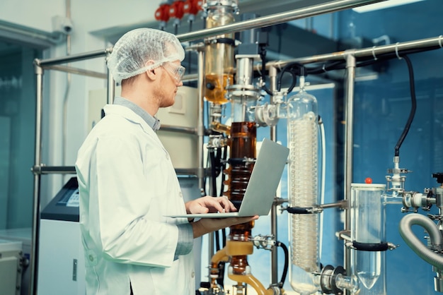 Apothecary scientist working with laptop near CBD oil extractor in laboratory