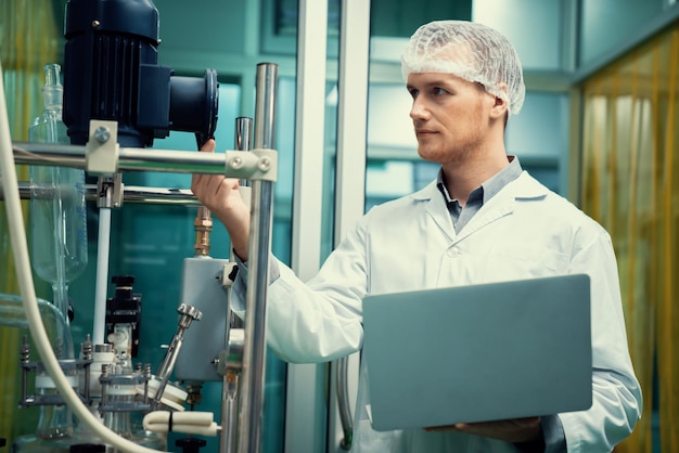 Apothecary scientist working with laptop near CBD oil extractor in laboratory