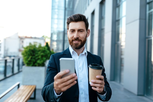 App for business and work Confident millennial attractive european businessman with beard in suit with coffee