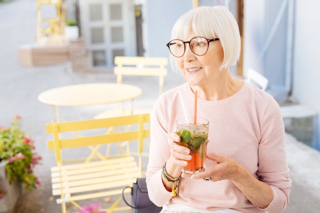 Appealing senior woman staring aside and holding drink