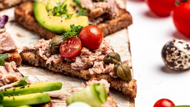 Appetizer bruschetta with tuna Italian bruschetta sandwiches with canned tuna tomatoes and capers toasts with tuna delicious healthy food on a dark background Top view flat lay