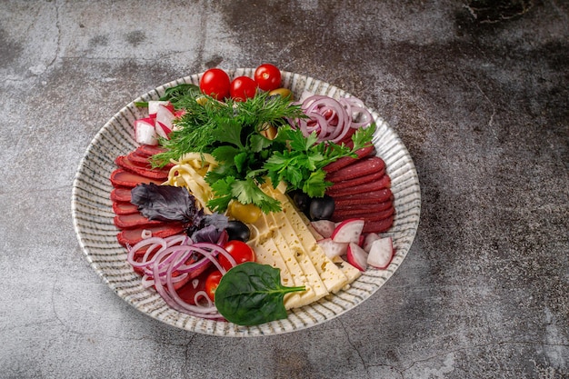 An appetizer in a restaurant, assorted meats. Sliced meat and sausage in layers on a plate with greens against a gray stone table