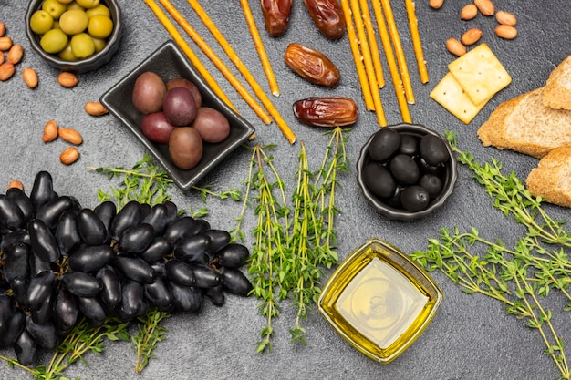 Appetizer set for aperitif with olives and cheese grapes and dates baguette and crackers nuts and thyme sprigs