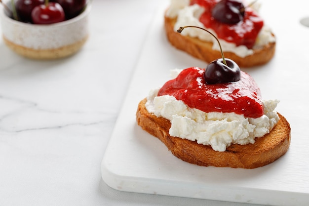 Appetizer with ricotta cheese cream cheese jam and cherry on white board and marble table Toast