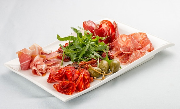 Appetizers of Italian sausages Prosciutto chorizo pancetta and salami Capers arugula and sundried tomatoes On white background