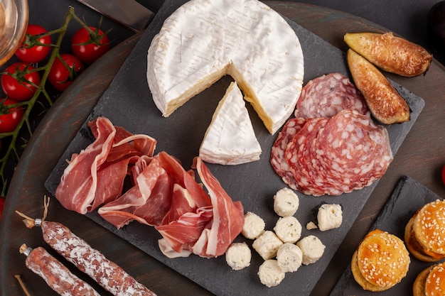 Appetizers table with diferents antipasti, cheese, charcuterie, snacks and wine. Mini burgers, sausage, ham, tapas, olives, cheese and baguette over grey concrete surface. Top view, flat lay