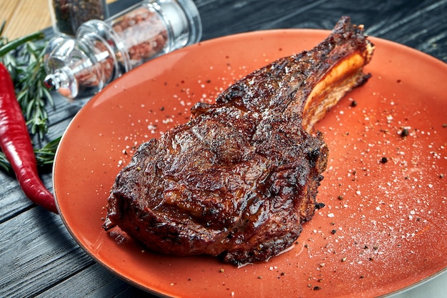 Appetizing aged beef club steak grilled served in a plate on a wooden, black surface. American BBQ culture