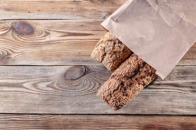 Appetizing baguettes with sesame seeds and nuts in a paper bag on a wooden background. Healthy Food Concept. Top view. Copy space