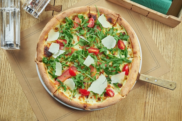 Appetizing baked pizza with salmon, cherry tomatoes, parmesan and arugula with crispy crust on a wooden table. Restaurant table setting. Top view