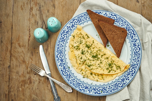 Appetizing breakfast - omelet with greens and rye toast on a ceramic plate on a wooden surface.