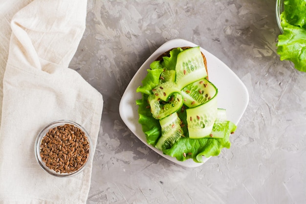 Appetizing bruschetta from rye bread lettuce cucumber and flax seeds on a plate and a bowl with grains on the table Healthy diet food Top view