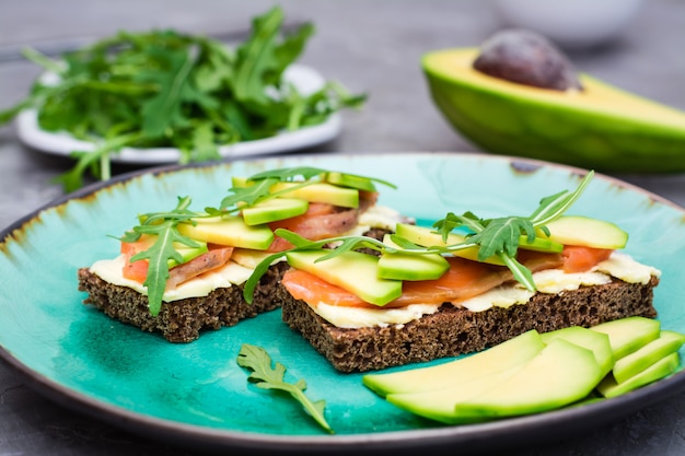 Appetizing bruschetta with salmon, butter, avocado and arugula on a plate