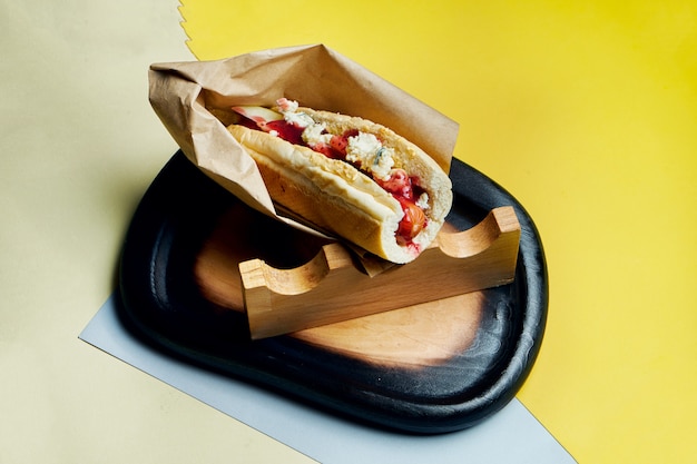 Appetizing classic American hot dog with caramelized onions, cheddar cheese, mustard and ketchup with a side dish of potatoes on a colored surface. Fast food