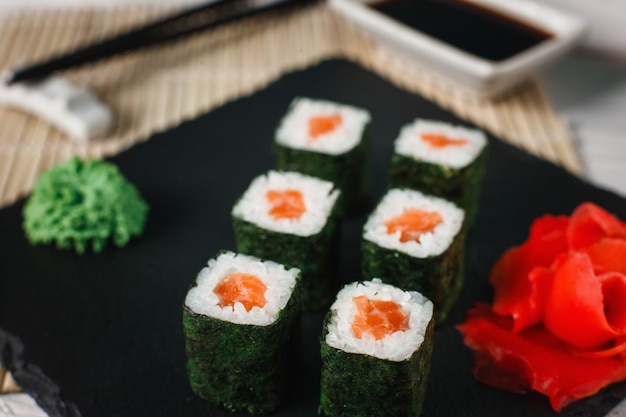 Appetizing, delicious and fresh sushi rolls set with smoked salmon served with ginger and wasabi on black slate. Japanese traditional cuisine, seafood.