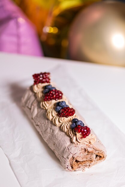 Appetizing dessert Meringue roll with blueberries and pomegranate against the background of airy bright balls