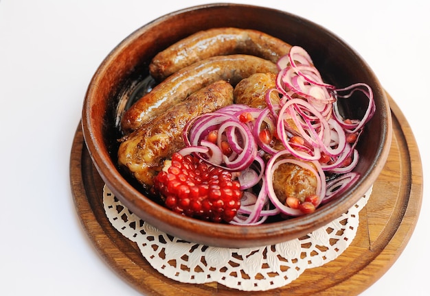 Appetizing fried sausages in a frying pan with blue onion rings and pomegranate seeds. Georgian or Caucasian kitchen