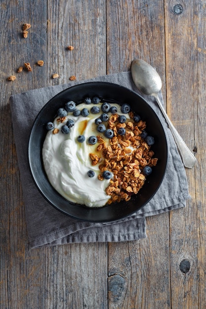 Appetizing homemade muesli with berries and yogurt served in bowl on wooden background.