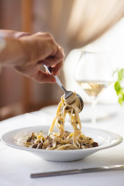 Appetizing Italian pasta with mushrooms on a light background. Man's hands with spoon and fork